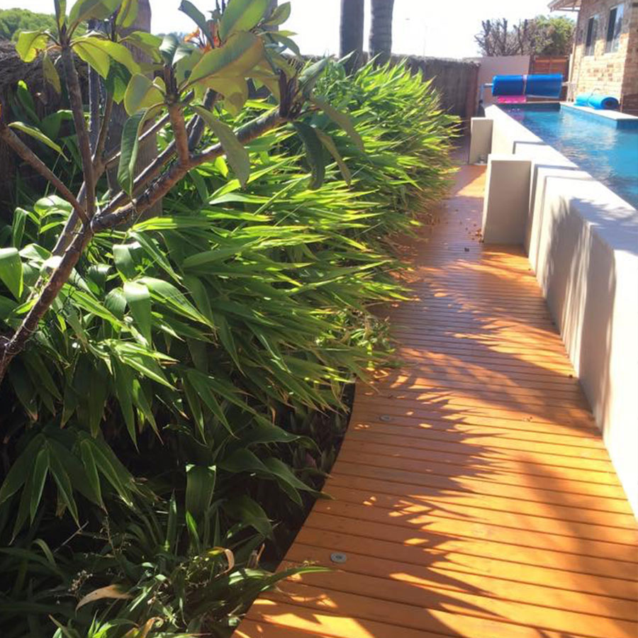 Timber-decked garden path leading to a paved poolside entertaining area