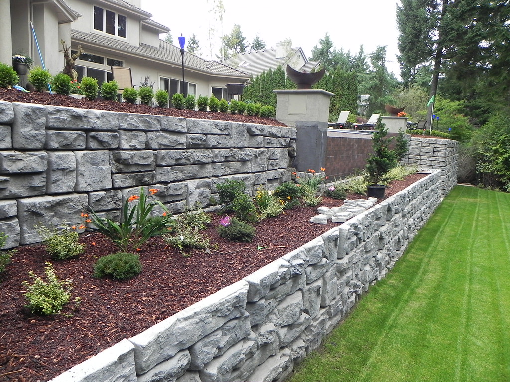 Stacked stone retaining wall with garden bed and manicured lawn